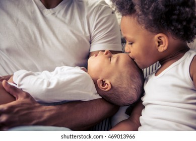 Beautiful young Afro American family spending time together. Little baby is sleeping in dad's arms while her sister is kissing her