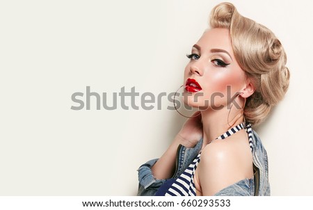 Beautiful young american girl in retro style, pinup. Blond, hairstyle - light curls. Retro make-up - red lips, black arrows. Clothing - jeans jacket and gold jewelry.