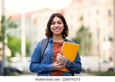 Beautiful Young Arab Female Student Standing Outdoors With Workbooks In Hands, Happy Attractive Middle Eastern Woman Posing Outside On City Street, Carrying Backpack And Smiling At Camera, Copy Space - Powered by Shutterstock