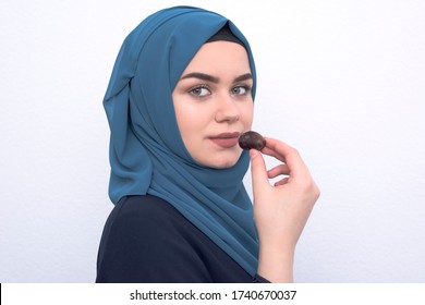 
A Beautiful Young Arab Muslim Girl With A Hijab Eating Dates On A White Background