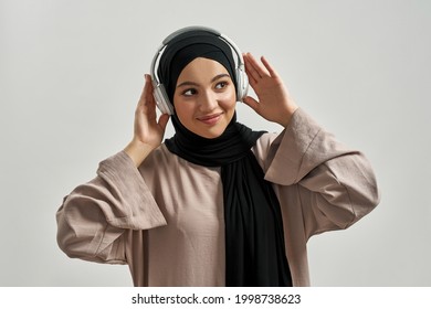 Beautiful young arabian girl in hijab and headphones looking sideways while posing on light background. Beautiful muslim lady - Powered by Shutterstock