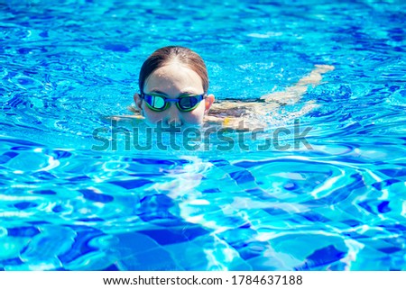 beautiful young armless woman training to swim in pool at tropical resort