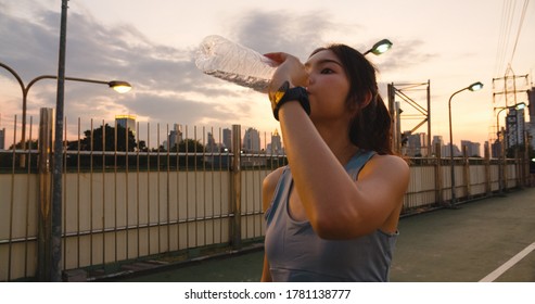 Beautiful Young Asia Athlete Lady Exercises Drinking Water Because Feel Tired After Running In Urban Environment. Japanese Teen Girl Work Out Wearing Sports Clothes On Walkway Bridge In Early Morning.