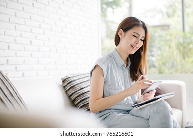 Beautiful young Asia woman working with smart phone in living room