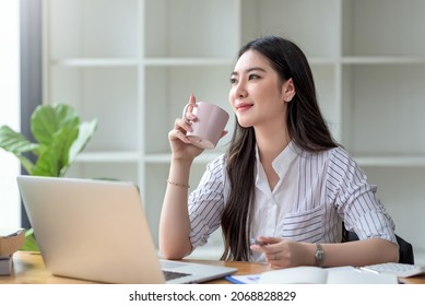 Beautiful young Asian businesswoman smiling holding a coffee mug and laptop working at the office. - Powered by Shutterstock