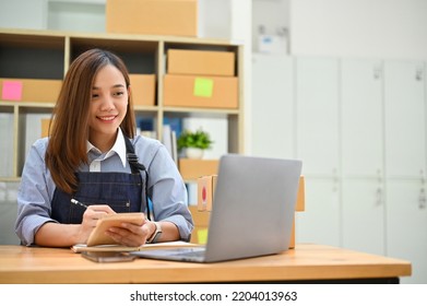 Beautiful Young Asian Female Business Startup Entrepreneur Or Online Small Shop Owner Working On Laptop Computer In Her Stock Room.