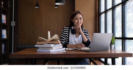 Beautiful Young Asian Female College Student In The Library Or Cafe Co-working Space Doing Her Homework And Using A Laptop Computer.
