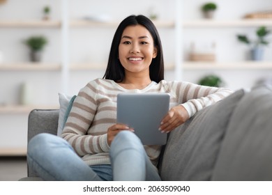 Beautiful Young Asian Female With Digital Tablet In Hands Posing On Couch At Home, Millennial Korean Woman Using Modern Device For Online Shopping Or Browsing Internet, Enjoying Domestic Leisure