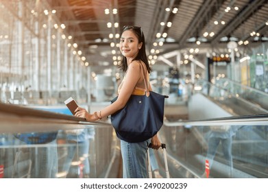 A beautiful young Asian female tourist passenger with her luggage is on the airport escalator, smiling at the camera, traveling by plane. people and transportation concepts, with copy space - Powered by Shutterstock