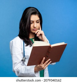 Beautiful Young Asian Girl Doctor, With A Book For Records Isolated On A Blue Background. Medical Student General Practitioner. The Concept Of Medical Education In India