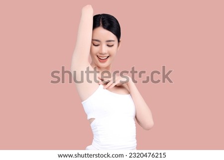 Beautiful young Asian girl lifting hand up to shows off clean and clear armpit or underarms isolated on pink background, Smooth and freshness armpit concept.