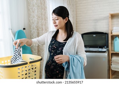 Beautiful Young Asian Japanese Pregnant Woman Doing Laundry At Home. Elegant Maternity Wife Holding Clean Clothes From Basket After Take Out From Washing Machine. Smiling Future Mom Do House Chores