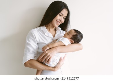 Beautiful Young Asian Mother And Cute Newborn Son In Her Arms. Loving Asian Mom Hug Embrace Small Baby Child, Relax Enjoy Tender Family Moment At Home. Beautiful Family, Mother's Day Concept.