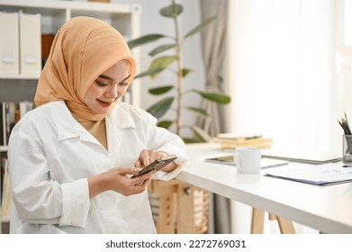 Beautiful young Asian Muslim businesswoman or entrepreneur wearing hijab and casual clothes using her phone in the office. - Powered by Shutterstock