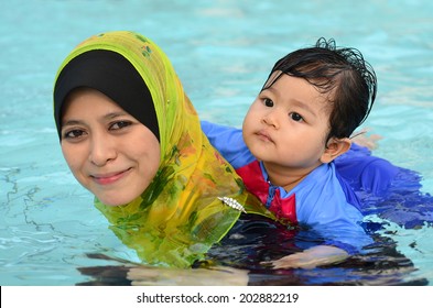 Beautiful young Asian muslim mother enjoying teaching her cute baby girl a first swimming lesson in a swimming pool - Powered by Shutterstock