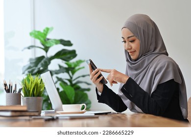 Beautiful young Asian muslim woman messaging or browsing social networks on her smart phone.