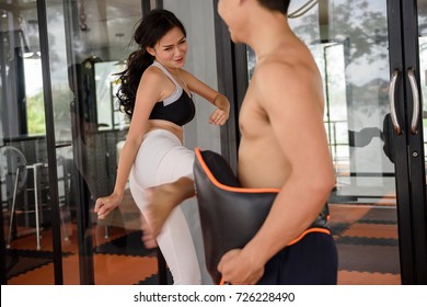 beautiful young Asian sporty slim white woman or girl , 20-30 years old. practice Muay Thai boxing by kicking at stomach Boxing Mitt held by Healthy trainer man at sport club.