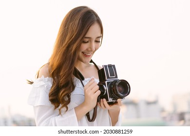 Beautiful young Asian stylish woman taking photos with retro film camera on the rooftop of a building. Asian girl smiling enjoy weekends, Holiday lifestyle trip. - Powered by Shutterstock