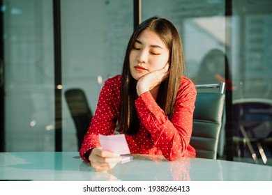 Beautiful Young Asian Thai Businesswoman In Red Shirt Reading Sticky Not Post It With Concern And Worried Expression.