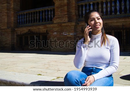 Beautiful young asian tourist. She is sitting resting on the steps of a square while talking on a mobile phone