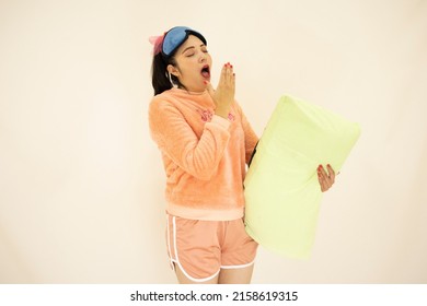 Beautiful Young Asian White Woman Wearing Pink Pajamas, Night Cap And Sleeping Mask, Standing Yawning And Closing Her Eyes, On White Background