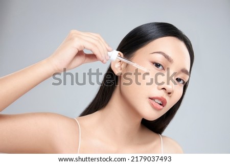 Beautiful young asian woman apply facial serum isolated on light grey background. Skin care and rejuvenation.