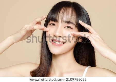 Beautiful young Asian woman with bangs and fresh smooth skin. Cute female model with natural makeup and sparkling eyes on beige background. Face care, Facial treatment, Cosmetology, beauty and spa.