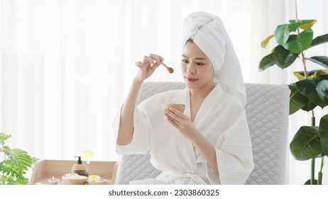 Beautiful young asian woman in bathrobe and towel turban holding honey bowl for spa treatment at home on weekend. Beauty concept - Powered by Shutterstock