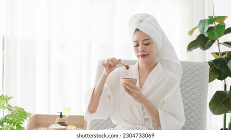 Beautiful young asian woman in bathrobe and towel turban holding honey bowl for spa treatment at home on weekend. Beauty concept - Powered by Shutterstock