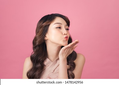 Beautiful young Asian woman blow a kiss on pink background - Powered by Shutterstock