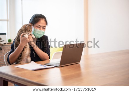 Beautiful young Asian woman with cat using notebook computer connect internet for video call meeting with friends at home during coronavirus pandemic outbreak for self isolation and social distancing.