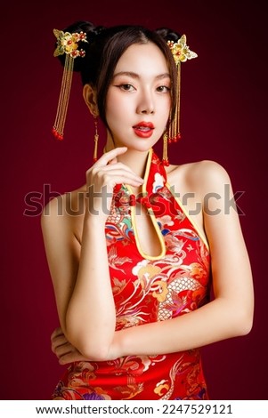 Beautiful young Asian woman with clean fresh skin wearing traditional cheongsam qipao dress posing on red background. Portrait of female model in studio. Happy Chinese new year.