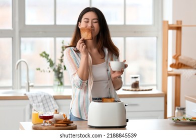 Beautiful young Asian woman with coffee and tasty toasts in kitchen - Powered by Shutterstock