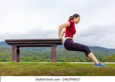 Beautiful young Asian woman doing tricep dips exercise outdoor at a park, cloudy sky and mountains background, healthy lifestyle