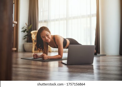 A Beautiful Young Asian Woman Doing Plank On Training Mat While Watching Online Workout Tutorials On Laptop At Home