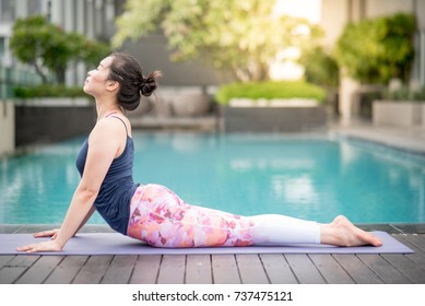 Beautiful young Asian woman doing yoga exercise with Bhujangasana posing (Cobra Pose) near swimming pool. Healthy lifestyle and good wellness concepts - Powered by Shutterstock