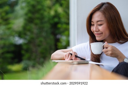A beautiful young asian woman drinking coffee and writing on a notebook in the outdoors