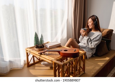 A Beautiful Young Asian Woman Enjoy Drinking Coffee And Listening To Music With Headphone At Home, Happiness And Relaxation Concepts