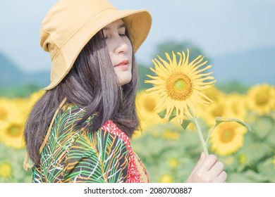 Beautiful young asian woman in a field of sunflowers in a colorful casual dress