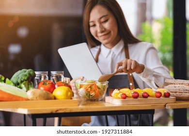 A Beautiful Young Asian Woman Following Recipe On Digital Tablet While Cooking Salad And Sandwich In The Kitchen, Online Learning Cooking Class Concept