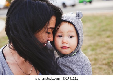 Beautiful young asian woman with freckles and her son outdoors. Mother brunette with dark hair holds her blond son in bear hood. Emotions on baby face. Unusual appearance, diversity, heredity concept - Powered by Shutterstock