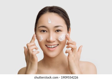 Beautiful young Asian woman gets cream in her face. The concept of skin care and hydration. a young woman with perfect clean skin health.