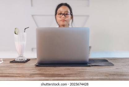 Beautiful Young Asian Woman With Glasses Using And Working On A Laptop Computer In A Cafe.
