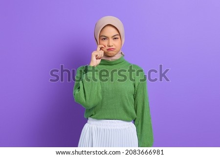 Beautiful young Asian woman in green sweater rubs tears wants to cry feels depressed has a problem isolated over purple background