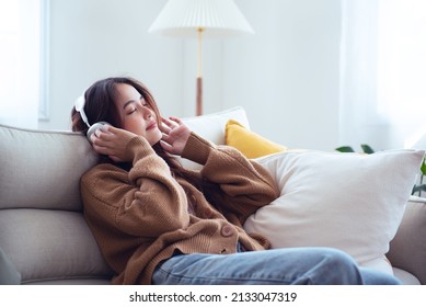 Beautiful Young Asian Woman With Headphones Relaxing And Listening To Music On The Sofa . Relax And Chill Out Concept.