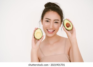 Beautiful young Asian woman with healthy glow perfect smooth skin and holding avocado in hands near the face isolated on white background. Skin care, beauty Natural, Healthy Lifestyle, Health Concept.