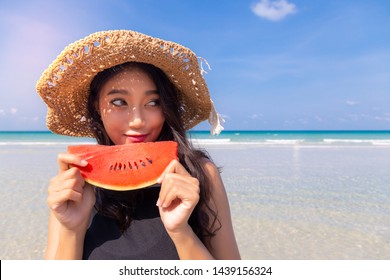 Beautiful young asian woman holding watermelon, looks at copy space in summer season at beautiful beach in hot weather that make beautiful Asia lady eat watermelon to cool down, quench her thirst
