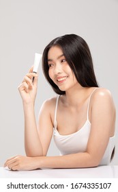 Beautiful Young Asian Woman Holding luxury white clean tube smile feeling so happy and cheerful with healthy Clean and Fresh skin,isolated on gray background,Beauty Cosmetics Concept