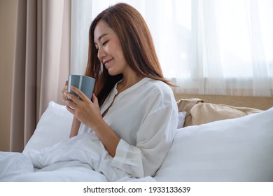 A Beautiful Young Asian Woman Holding And Drinking Coffee In A White Cozy Bed At Home