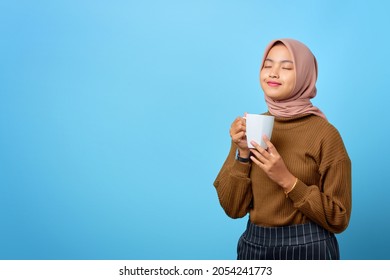 Beautiful young Asian woman holding mug and drinking tea on blue background - Powered by Shutterstock